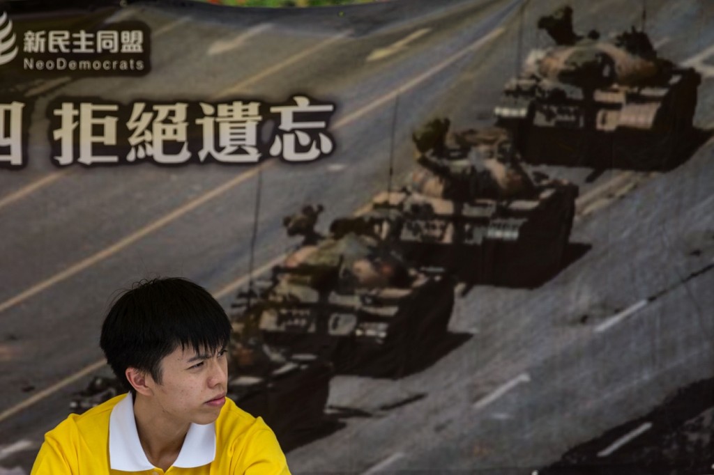 An activist sits in front of a poster of the "Tank Man" photo at his stall in Hong Kong on June 4, 2016, ahead of the commemoration of the bloody Tiananmen Square crackdown in 1989. / AFP / ANTHONY WALLACE