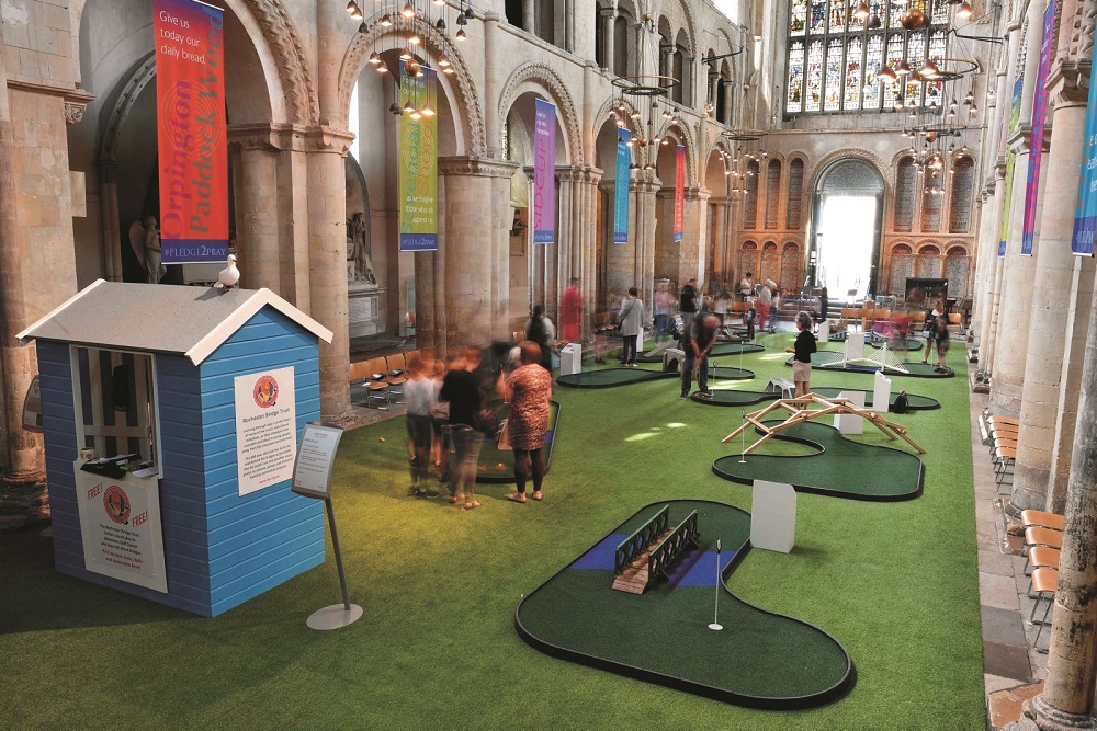 (FILES) In this file photo taken on August 6, 2019 people play on the bridge-themed mini-golf course set up in the nave of Rochester Cathedral in Rochester, south-east England. - A mini-golf course in the nave of a mediaeval English cathedral to encourage families to visit this summer is proving a match made in heaven -- and controversy. (Photo by Ben STANSALL / AFP)