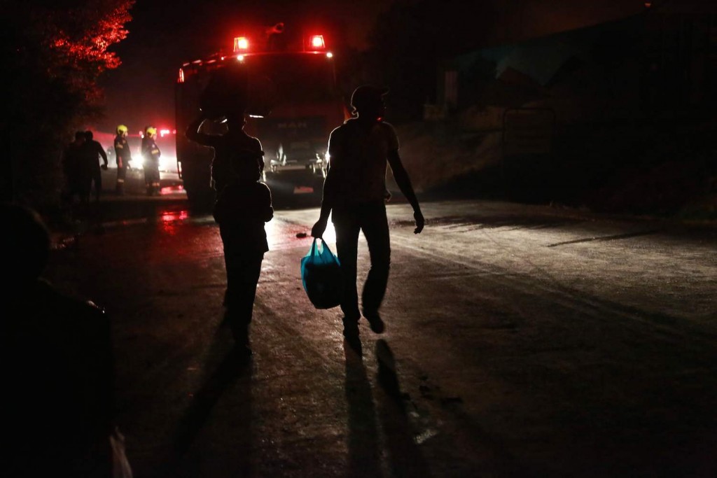 TOPSHOT - Migrants leave as a fire burns in the Moria camp on the island of Lesbos on September 9, 2020. (Photo by Manolis LAGOUTARIS / AFP)